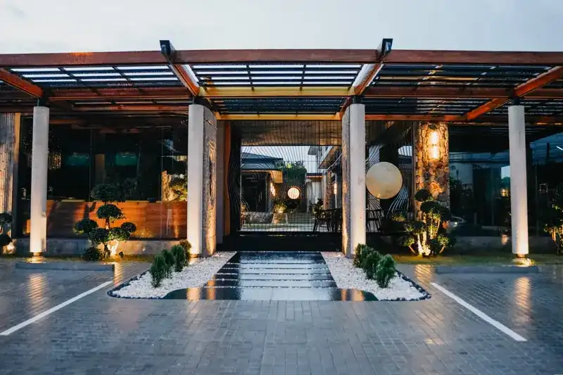 The entrance at dusk: a long timber pergola, stone pillars and a reflecting pool