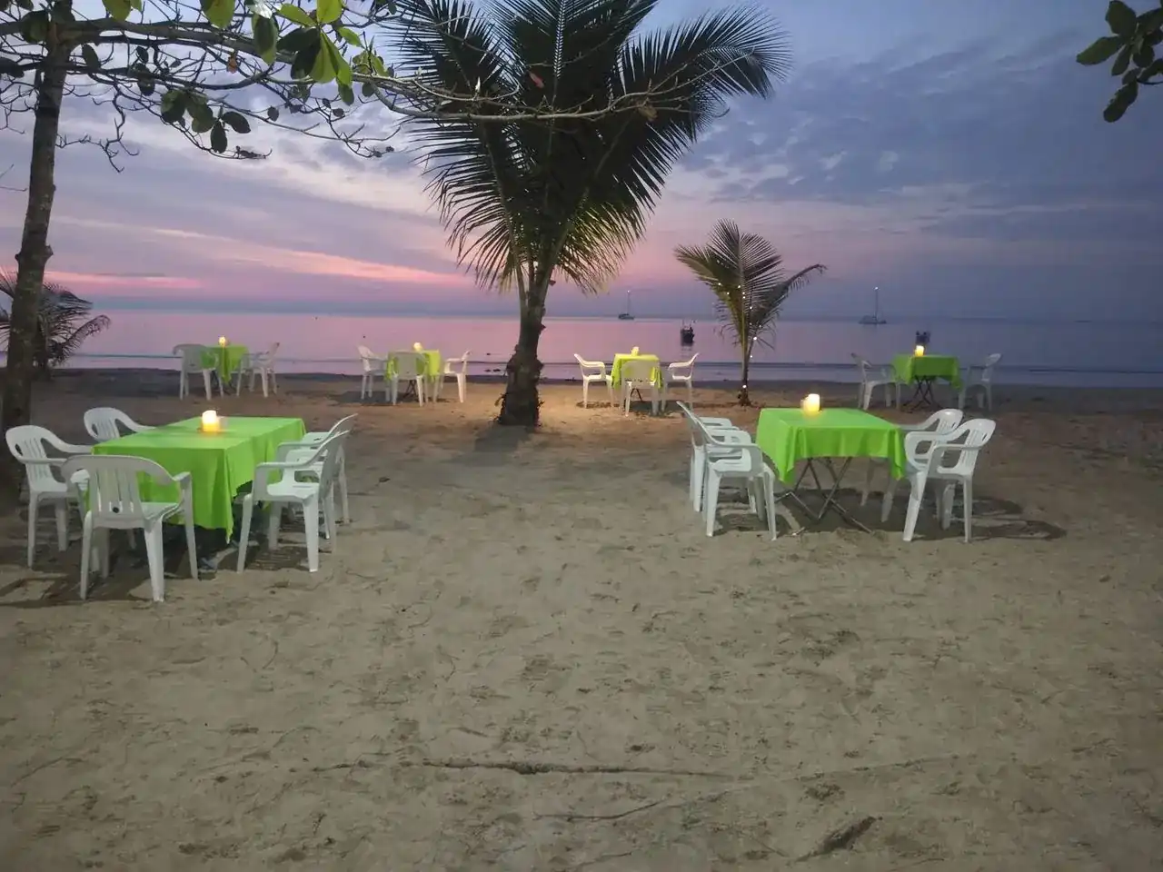 Tables with green cloths and small lights on the sand at Nai Yang Beach, under a pink evening sky