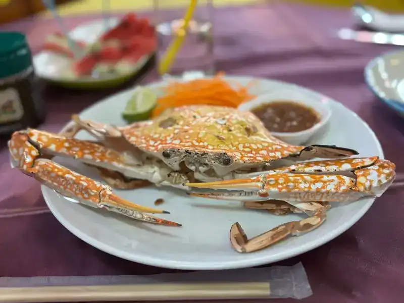 A whole blue crab with a dipping sauce, lime and shredded carrot