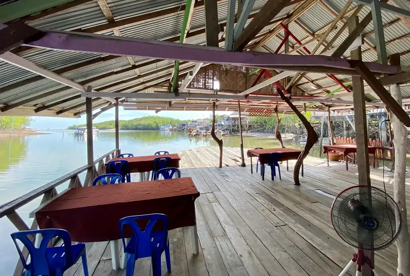 Open wooden deck under a tin roof, tables with maroon cloths and blue chairs, looking out over the water to the mangroves