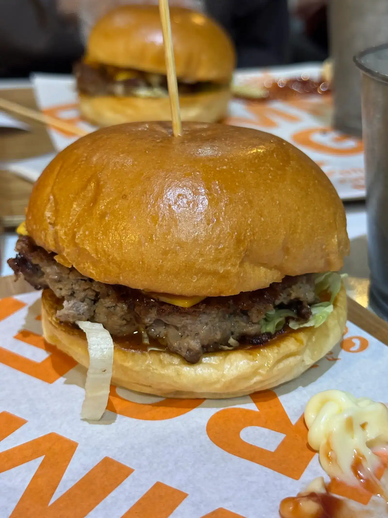 A smash burger in a glossy bun on the restaurant's orange-lettered paper / เบอร์เกอร์เนื้อสแมชในขนมปังเงาวาว บนกระดาษลายตัวอักษรสีส้มของร้าน