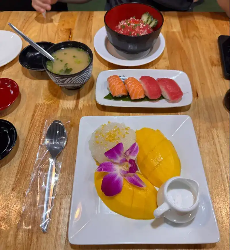 Salmon and tuna nigiri, miso soup and a rice bowl, next to mango with sticky rice and an orchid