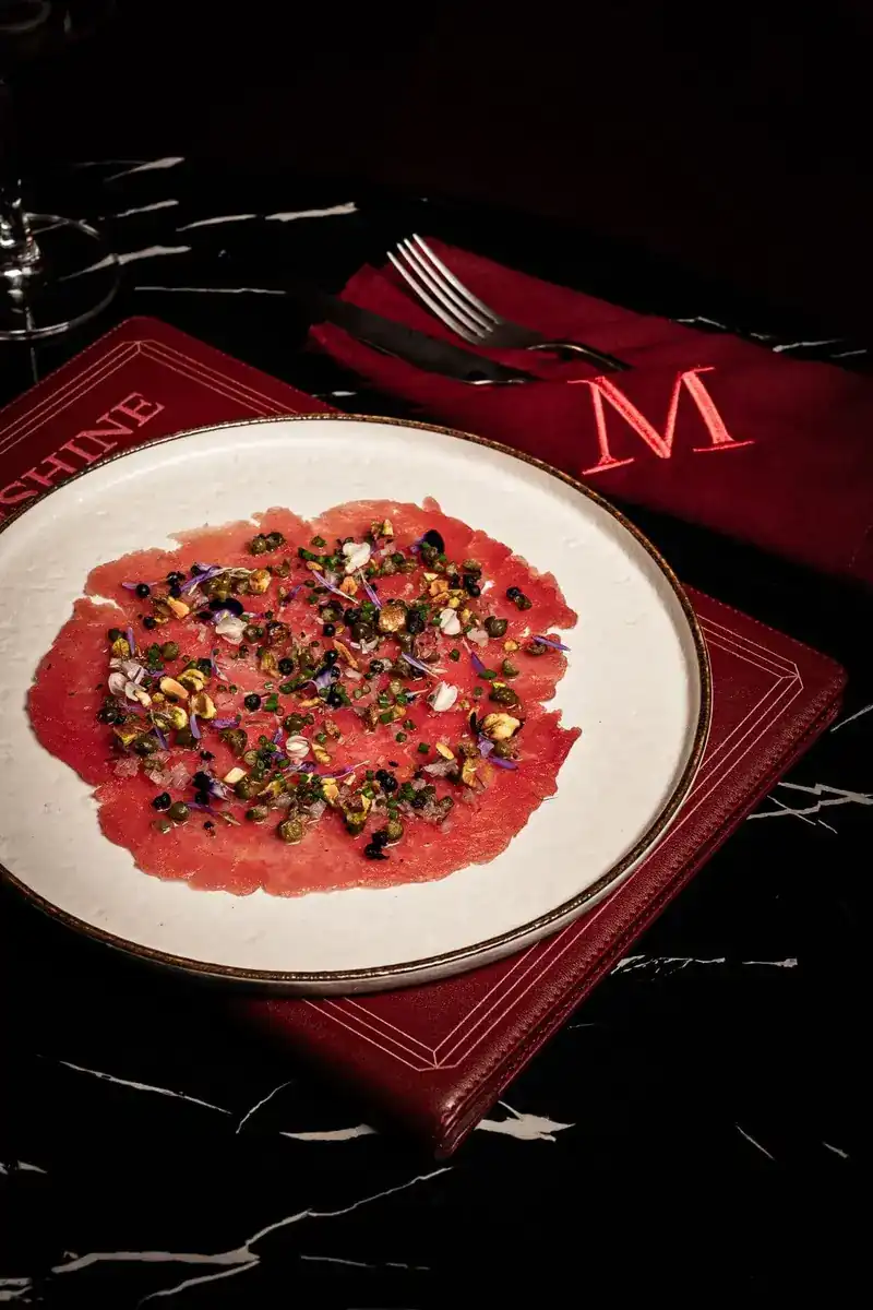 Tuna carpaccio with capers and pistachios on a white plate