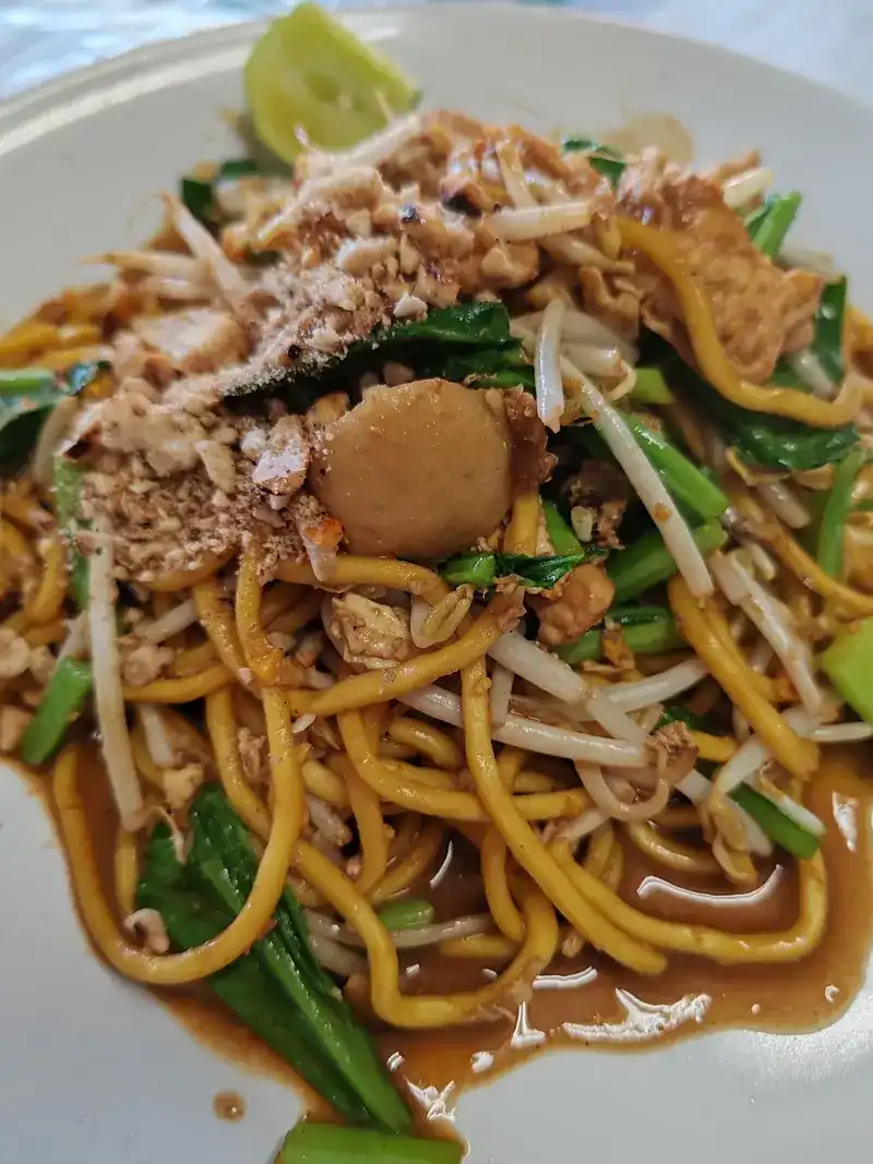 Fried yellow noodles with bean sprouts, greens, crushed peanuts and lime
