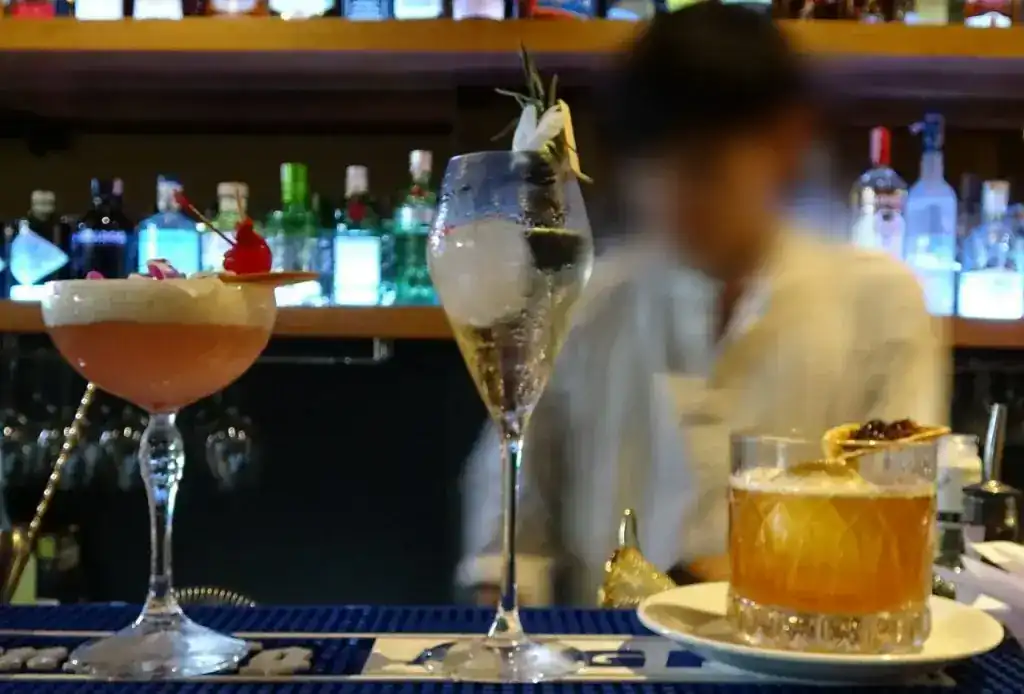 Two cocktails on the bar counter at Little Lillo, one in a coupe glass with a cherry, one in a tall glass with rosemary