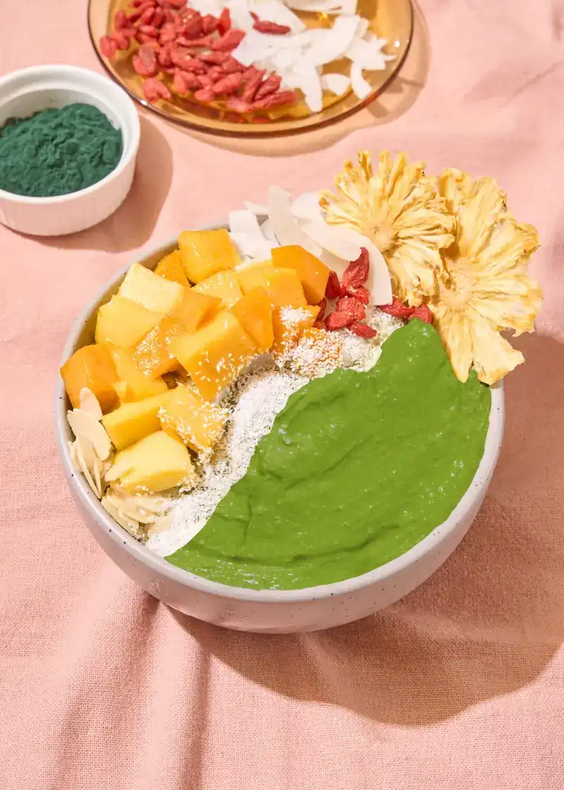 Green smoothie bowl topped with mango, coconut and dried pineapple flowers