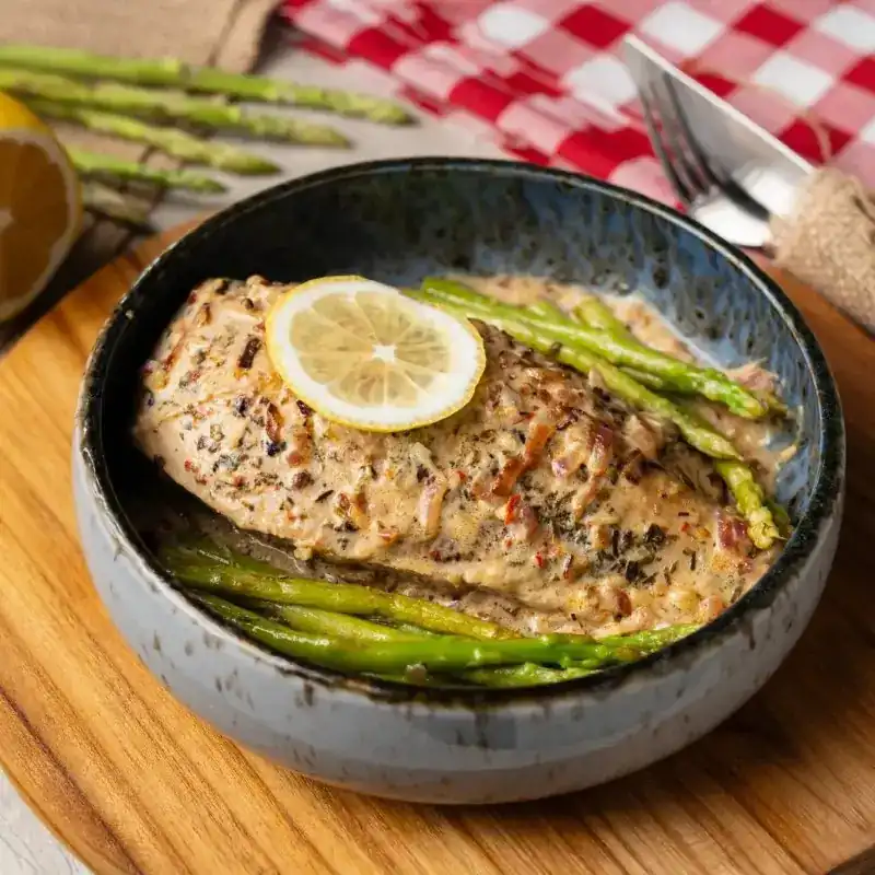 A bowl of creamy herb sauce with asparagus and a slice of lemon