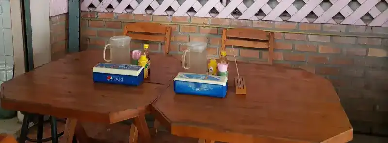 Two wooden tables with water jugs and sauce bottles against a brick wall under the pink lattice