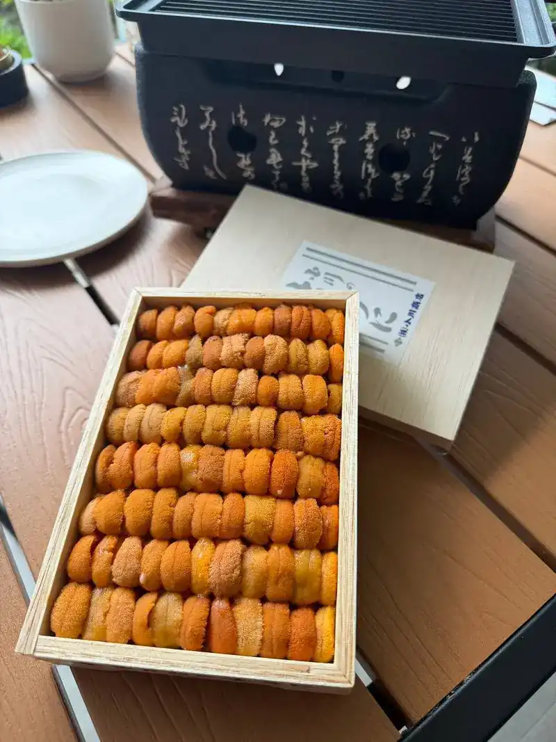 A wooden box filled with sea urchin, next to a tabletop grill