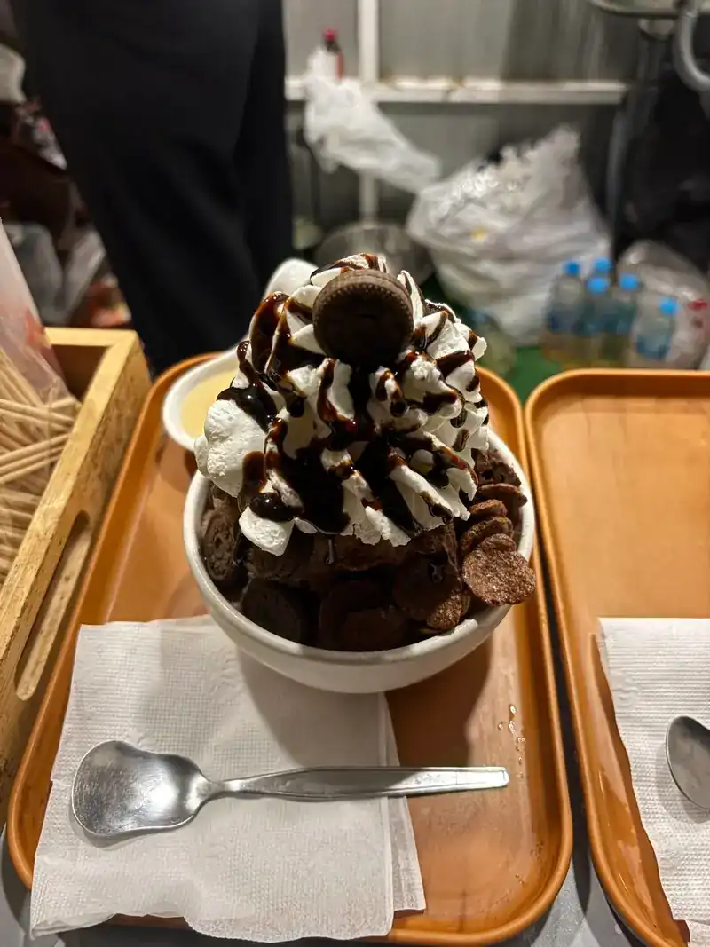 A chocolate dessert bowl piled with whipped cream, chocolate sauce and small cookies, on a wooden tray