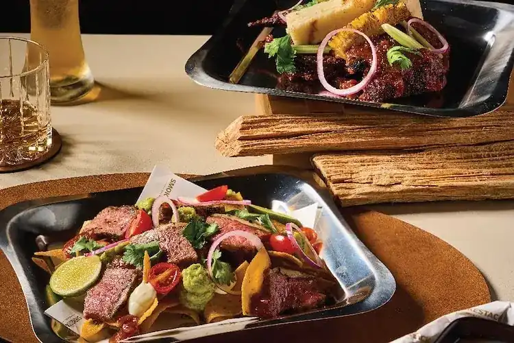 Tortilla nachos topped with sliced beef, with grilled chicken and corn behind