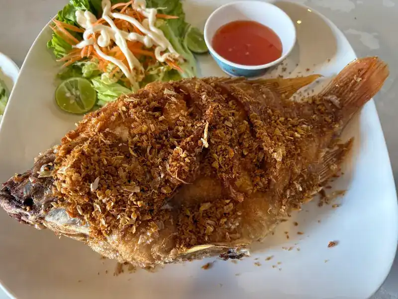 A whole fried fish covered in crispy garlic, with salad and sweet chilli sauce