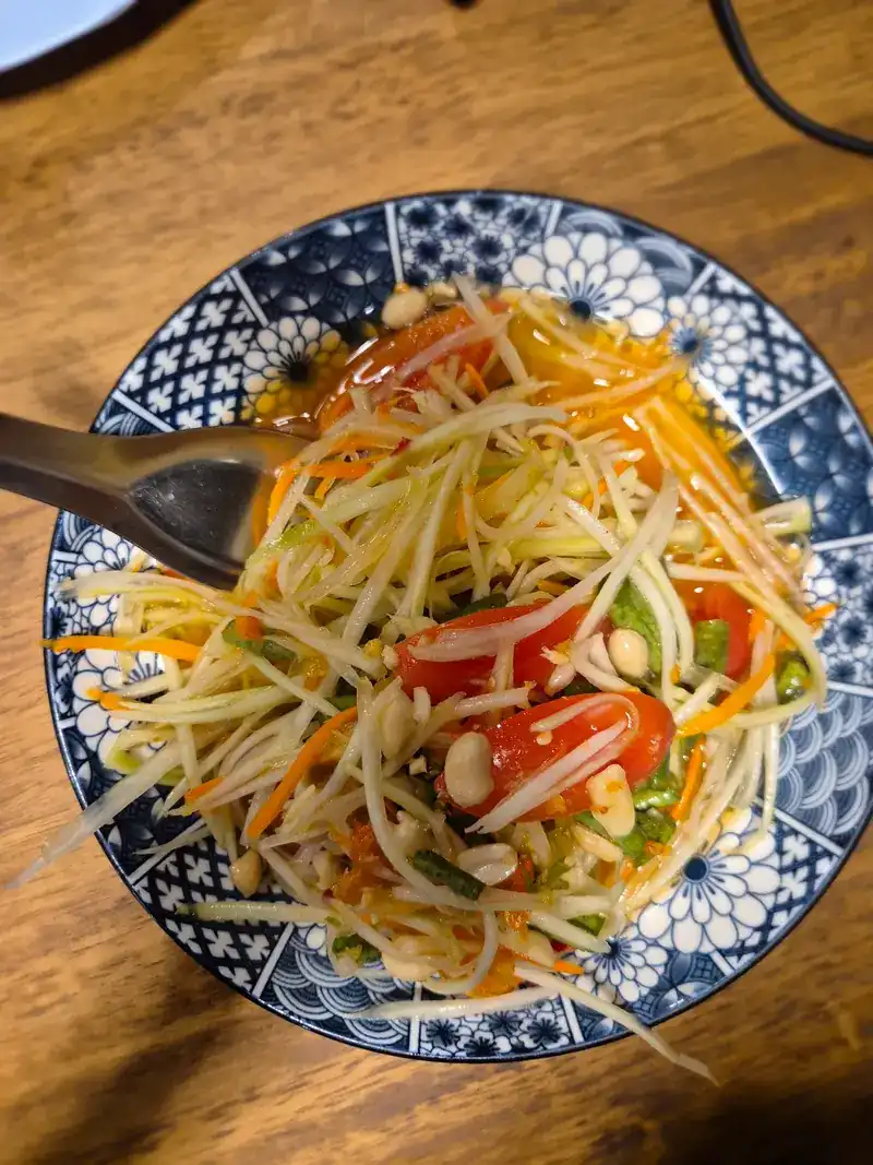 Green papaya salad with tomato and peanuts in a blue-and-white bowl / ส้มตำใส่มะเขือเทศและถั่วลิสงในชามลายคราม