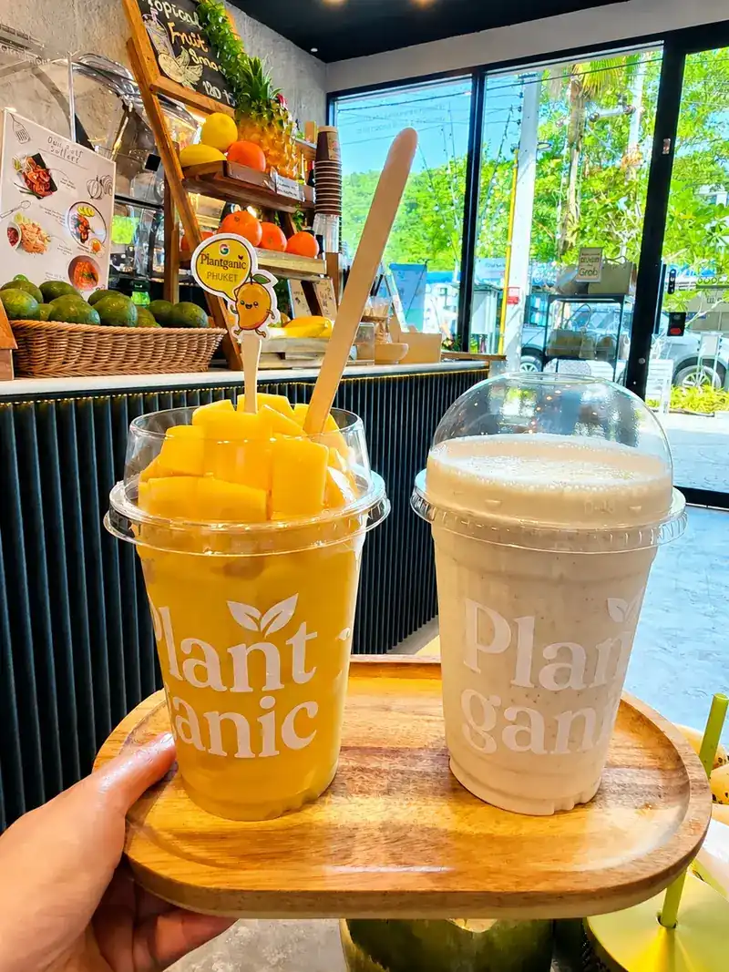 Mango smoothie topped with fresh mango, beside a second smoothie on a wooden tray