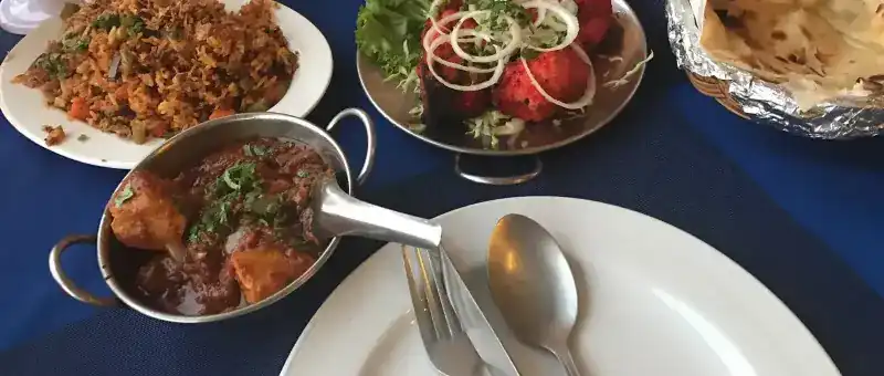 A table with rice, a curry, roast chicken under onion rings and naan