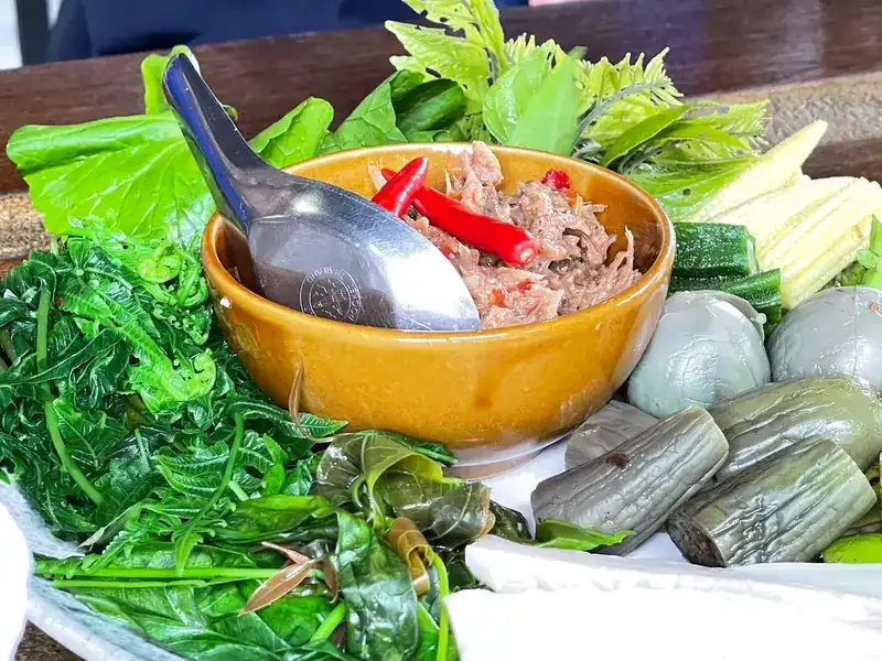 A chilli dip in an amber bowl, surrounded by fresh and blanched vegetables