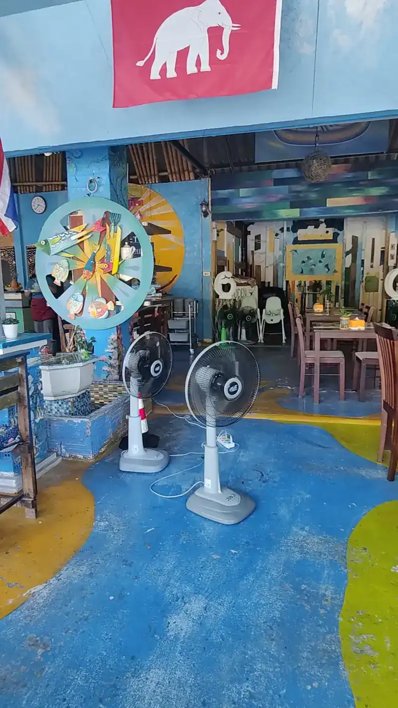 Blue painted floor with pools of yellow and green, standing fans, a white-elephant flag and the wheel of wooden fish