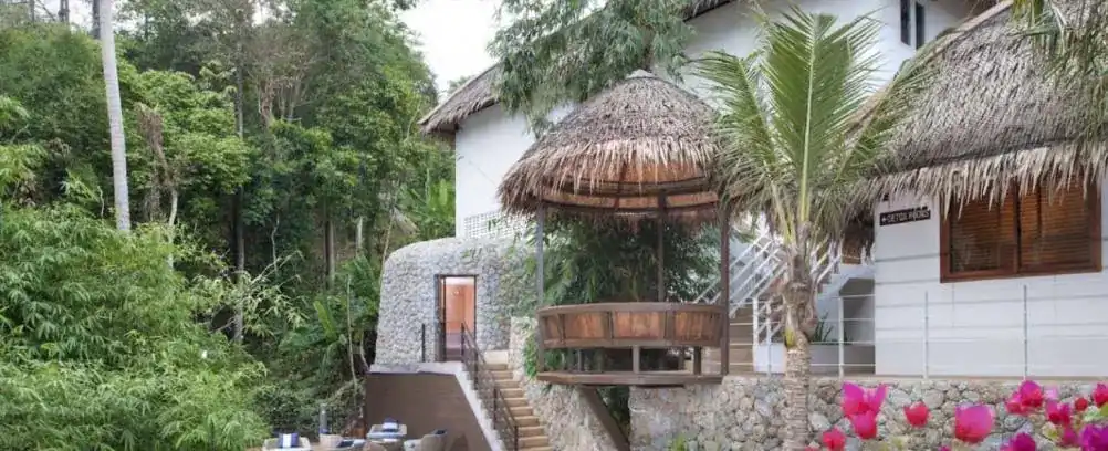 White buildings with thatched roofs and a round wooden pavilion among palms and jungle at Santosa