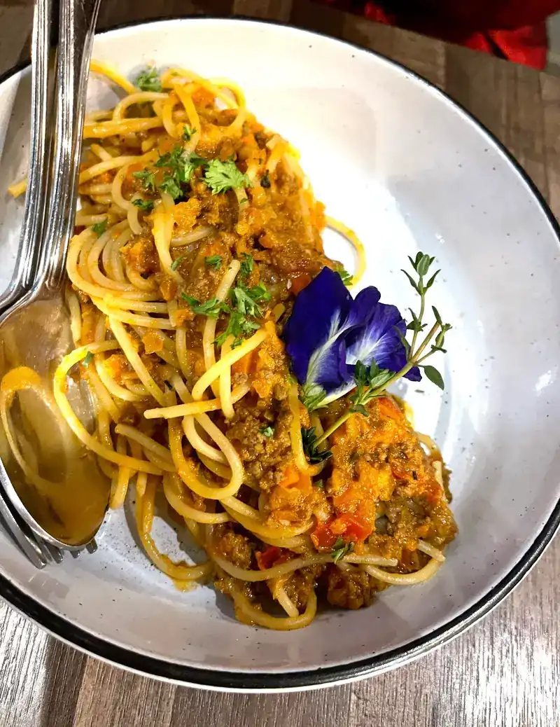 Spaghetti bolognese topped with herbs and a blue butterfly pea flower
