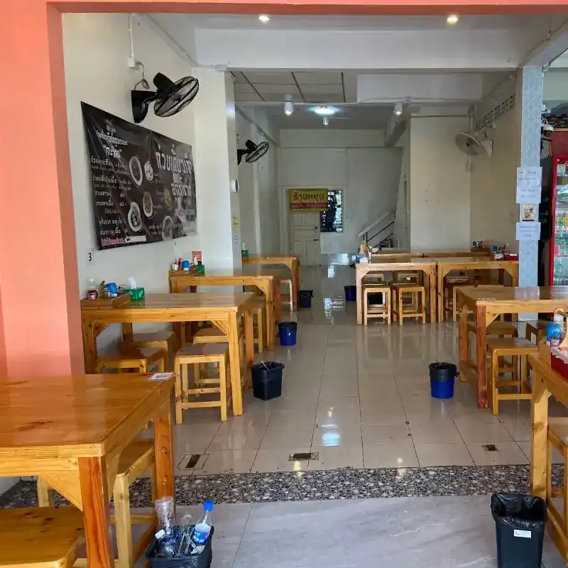 Inside the shop: rows of wooden tables and stools, wall fans and an orange wall at the front
