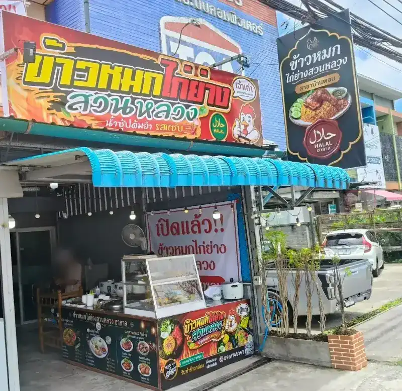 The shopfront: a red and yellow sign with a cartoon chicken, a blue awning, a green hanging sign and the food counter