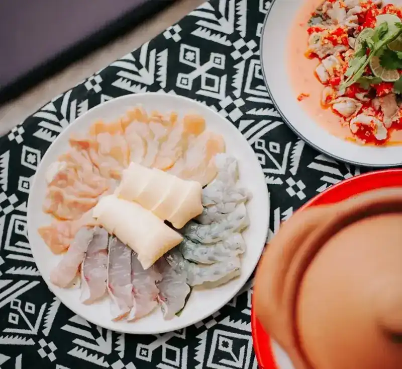 A plate of sliced fresh seafood beside a spicy seafood salad, on a black-and-white cloth