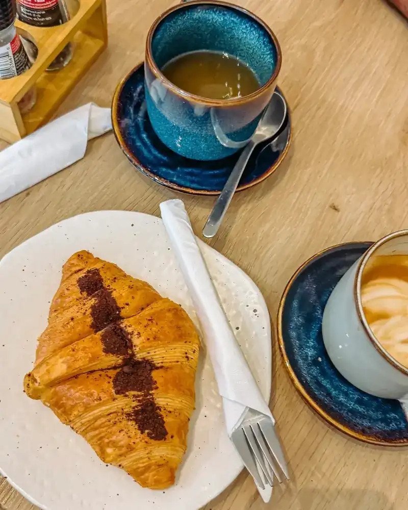 A croissant with two coffees in blue cups