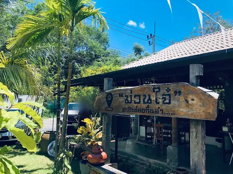 The carved wooden sign at the entrance, under palms, in front of the open wooden dining room