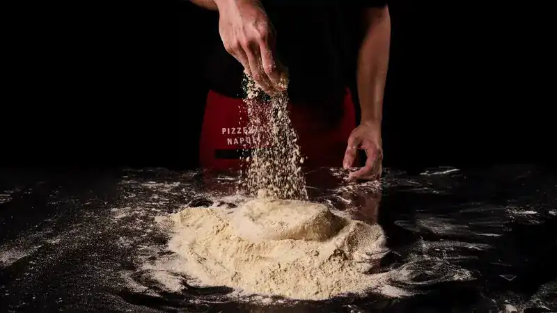 A hand dusting a mound of flour on the black bench