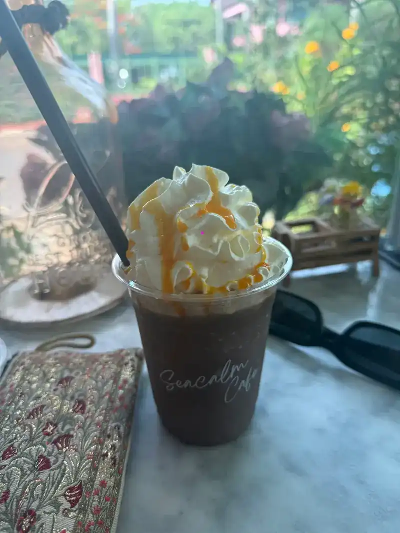 An iced chocolate drink in a Sea Calm cup, topped with whipped cream and caramel