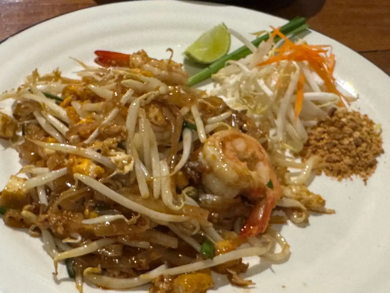 Pad thai with prawns, bean sprouts, crushed peanuts and a wedge of lime on a white plate