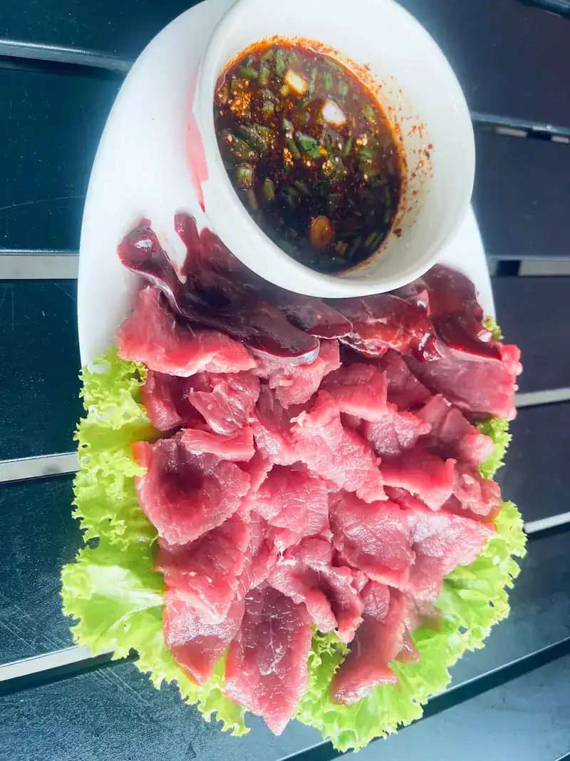 Thin slices of raw meat on lettuce with a bowl of chilli dipping sauce