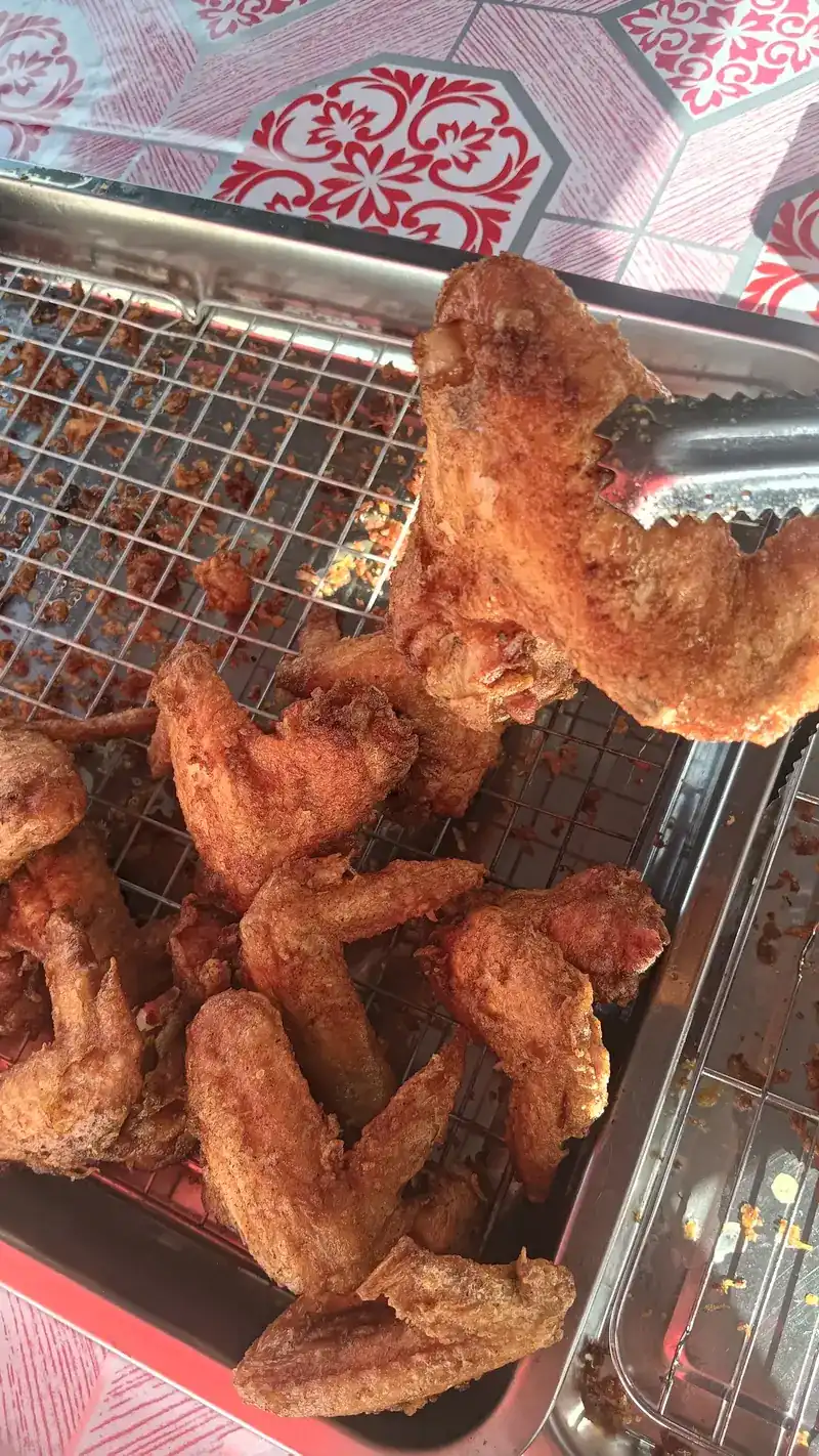Fried chicken wings on a wire rack, one lifted with steel tongs