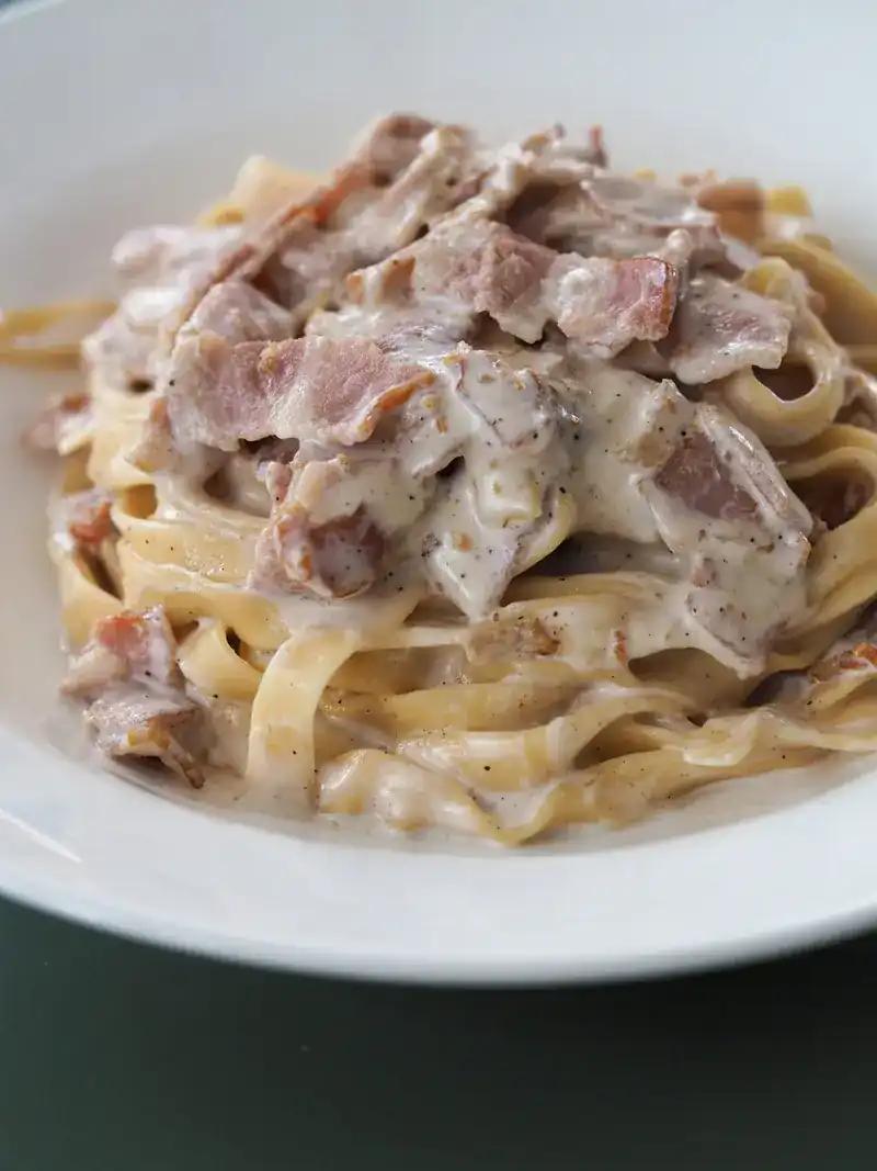Ribbon pasta in cream sauce topped with slices of bacon