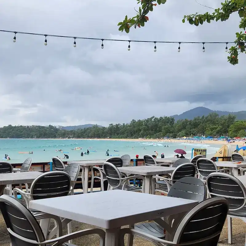 White tables on the terrace by day, with Kata Beach and the green hills behind