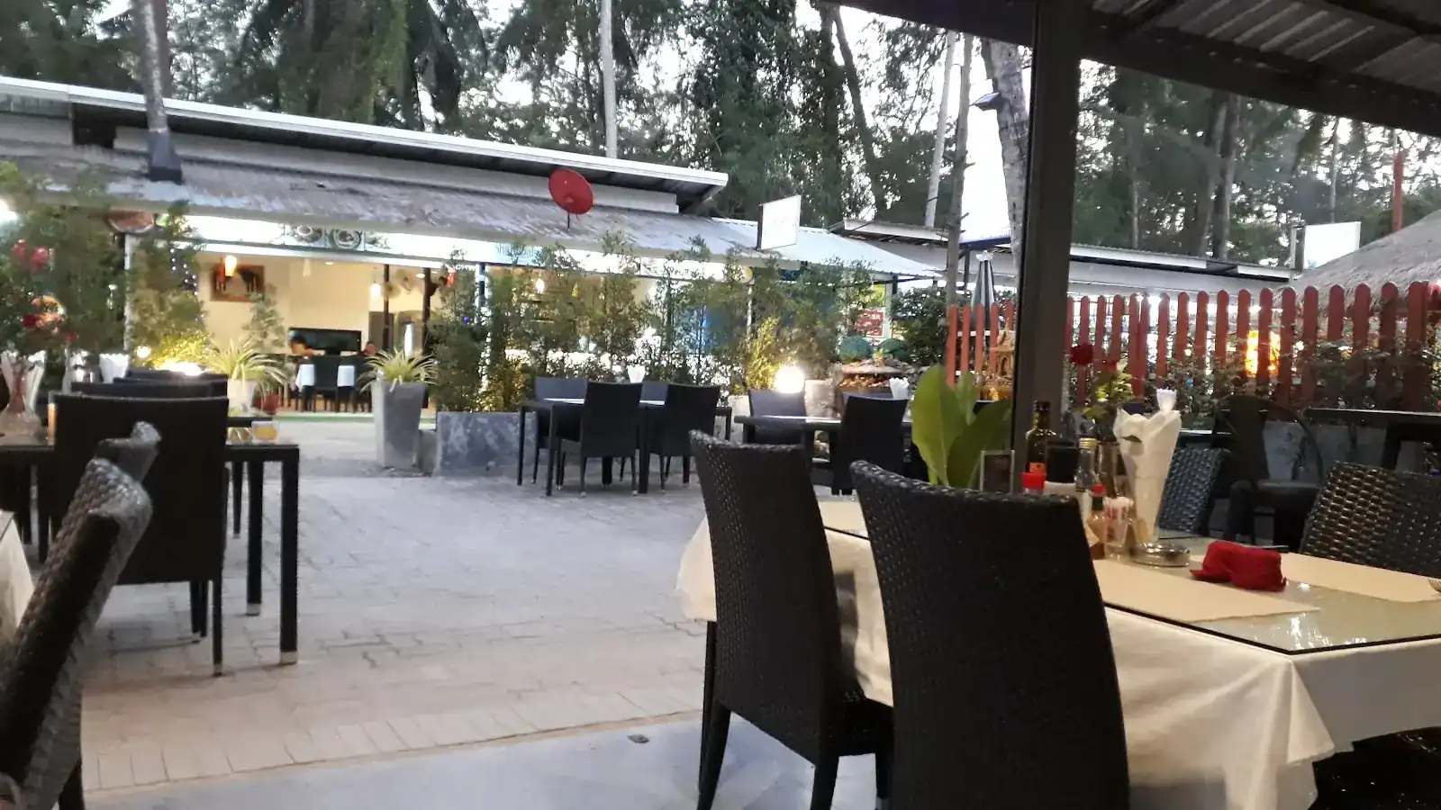 The outside tables at dusk, with wicker chairs, white cloths and lights in the garden