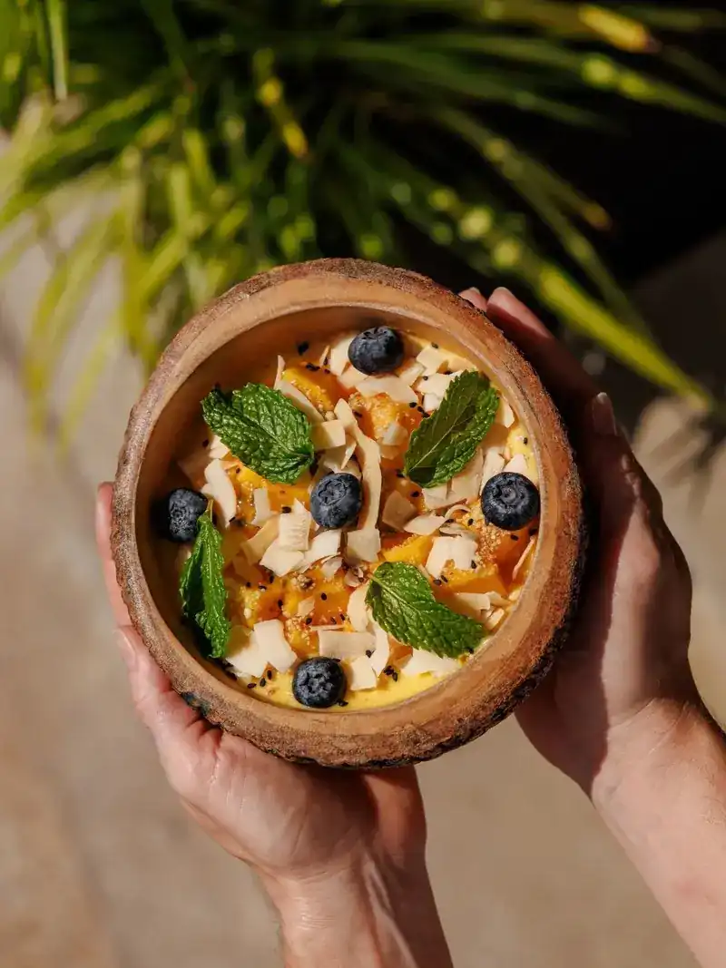 A smoothie bowl in a coconut-wood bowl with blueberries, mint and coconut chips
