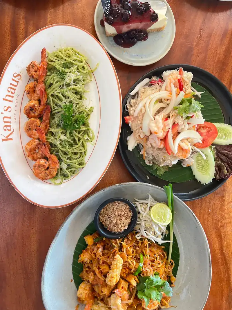 A table from above: shrimp with pesto spaghetti, a seafood salad, pad thai and a blueberry cheesecake