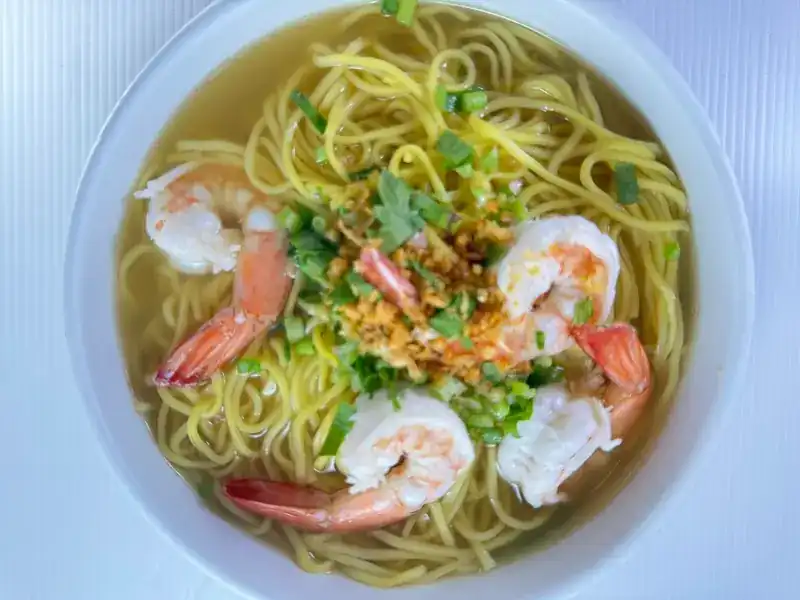 Yellow noodle soup with prawns, spring onion and fried garlic