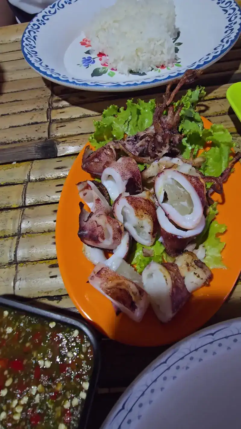 Grilled squid on lettuce with a bowl of dipping sauce, on a bamboo table