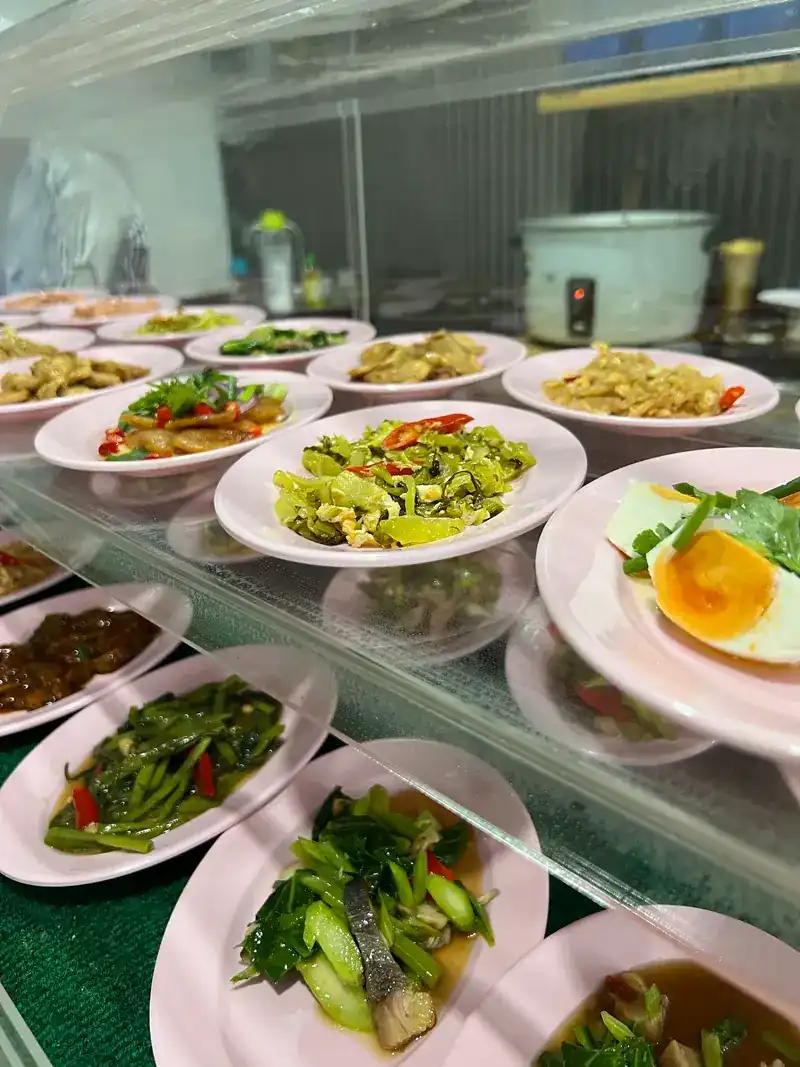 Close up of plates in the counter: stir-fried greens and a halved boiled egg, the rice pot behind