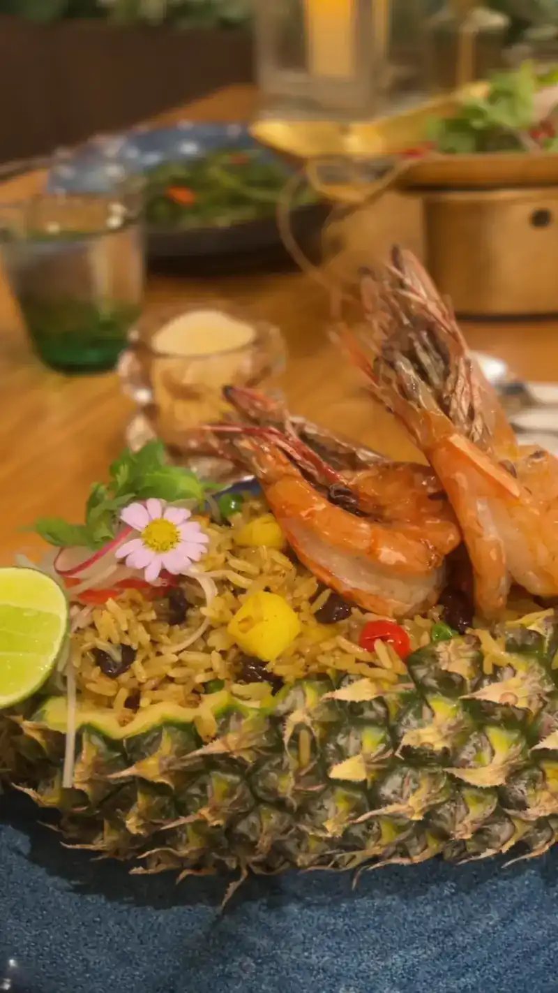 Fried rice served in a pineapple, topped with prawns, a flower and a wedge of lime