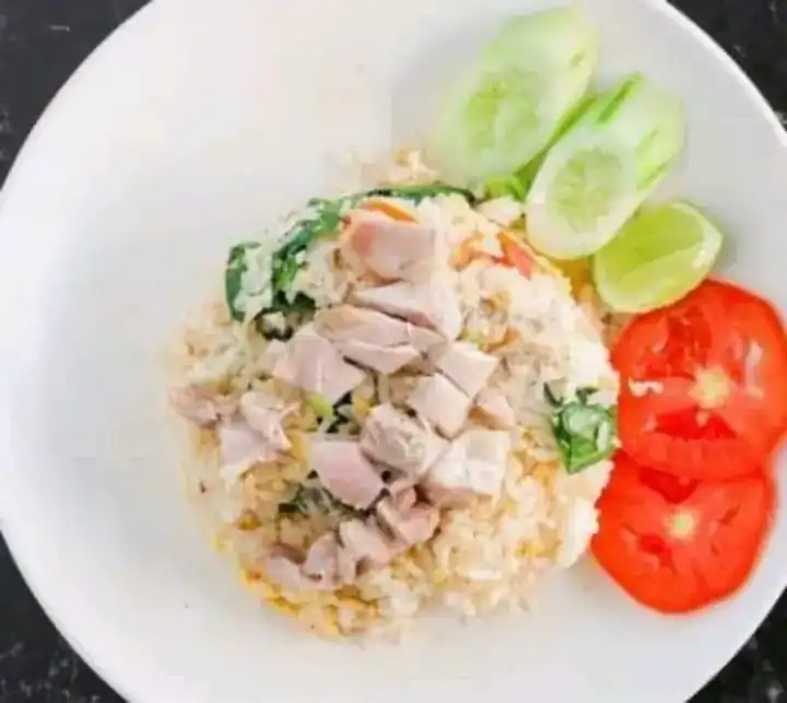 A plate of fried rice with cucumber, lime and sliced tomato on the side