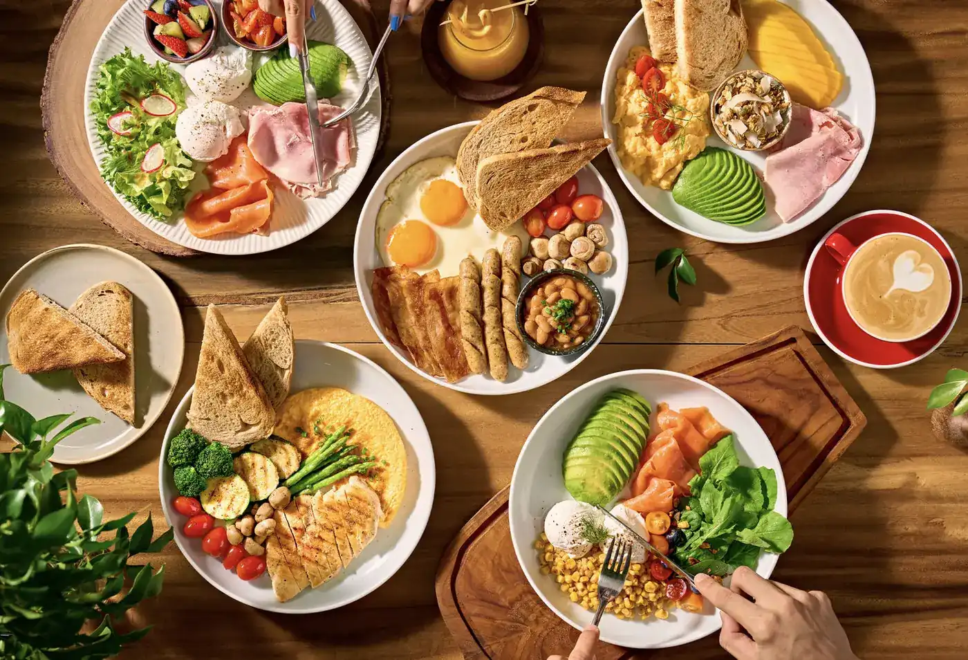 A wooden table seen from above, set with breakfast plates, toast and a latte