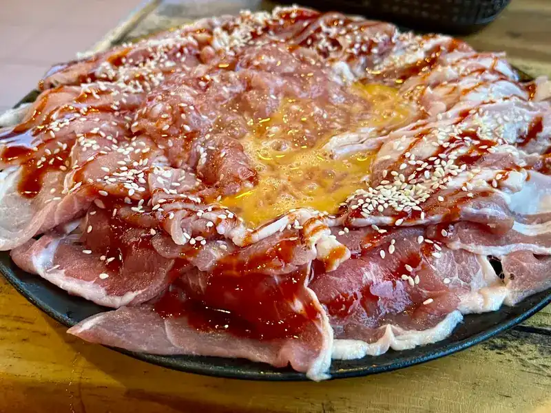 A round plate of sliced pork with a sweet glaze, sesame seeds and an egg yolk in the middle