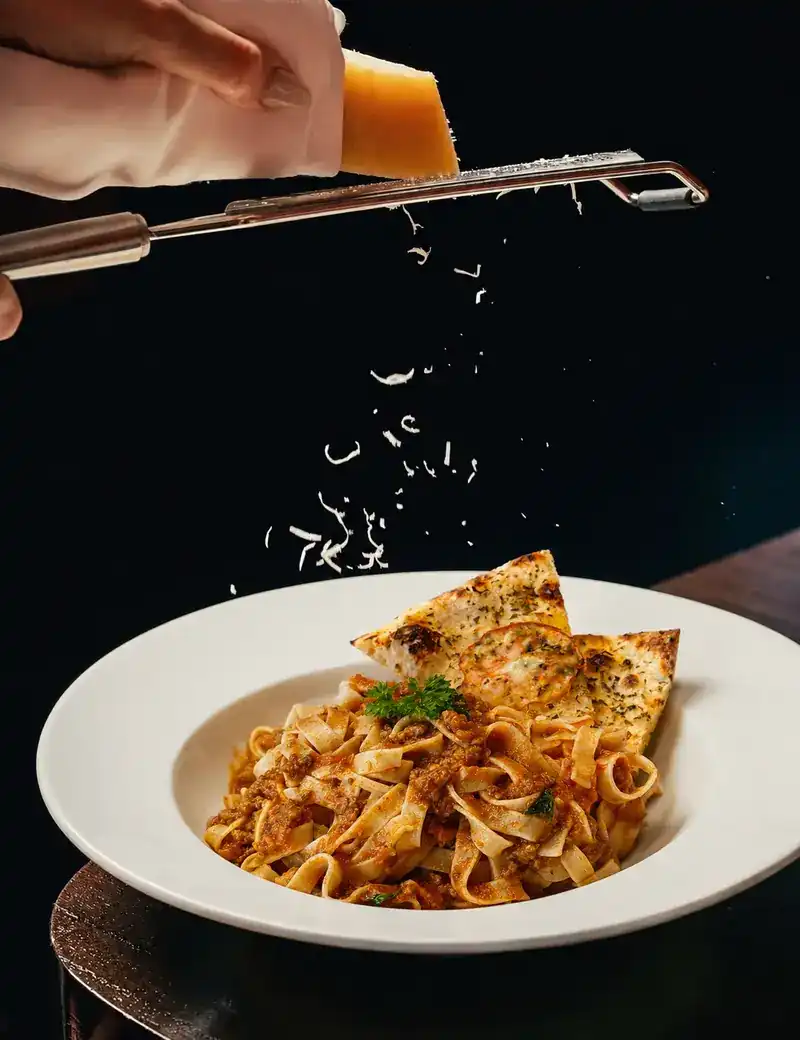 Hard cheese grated over a plate of ribbon pasta in a red sauce, with toasted bread on top