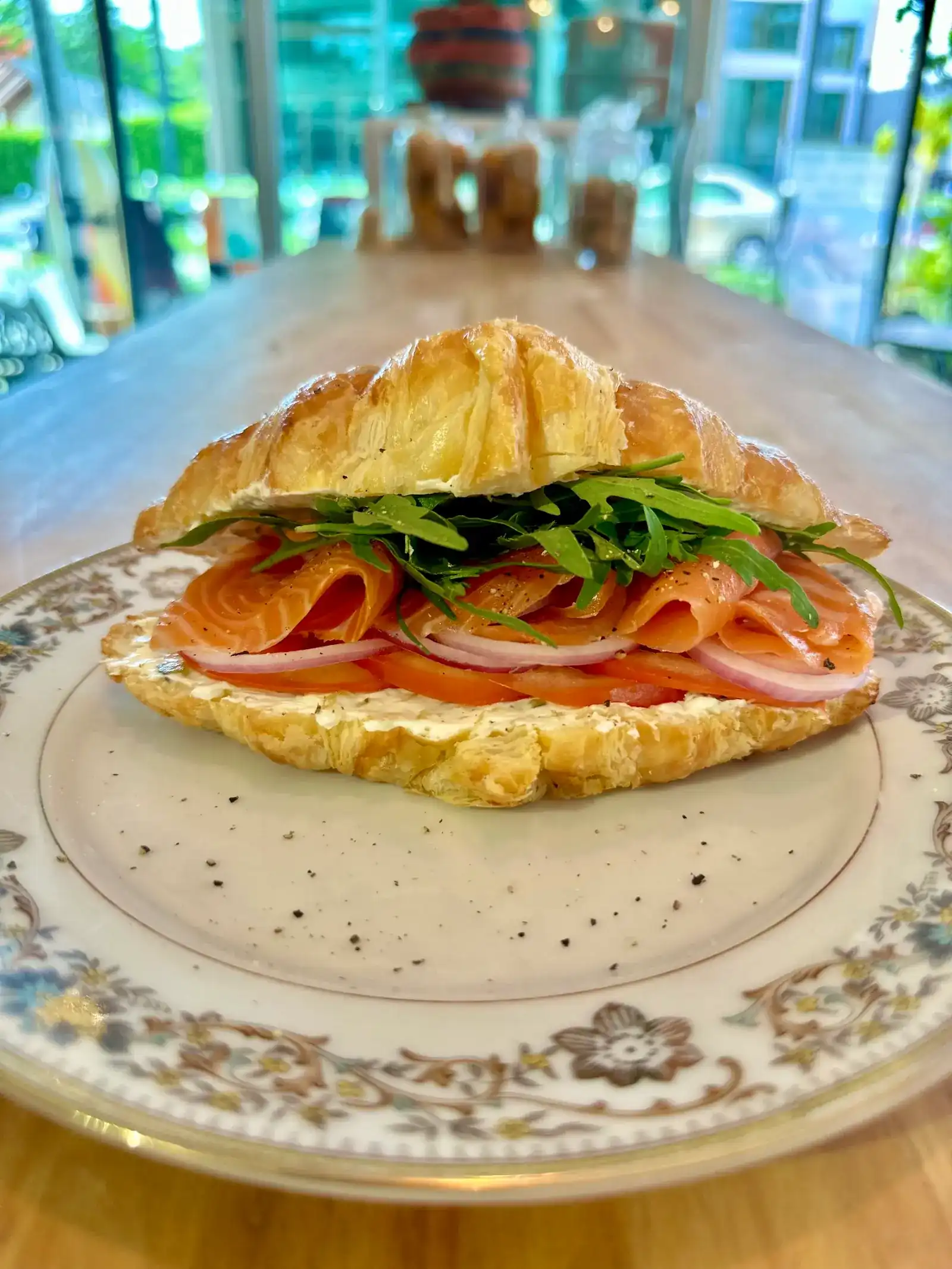 Smoked salmon croissant with rocket and red onion on a flowered plate