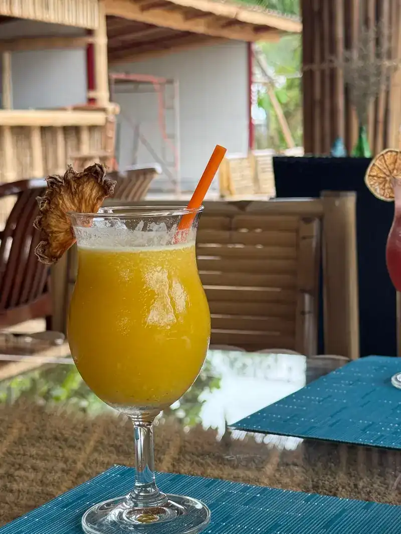 A tall glass of fruit drink with a dried pineapple slice and an orange straw