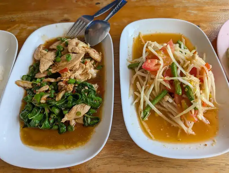 Stir-fried chicken with greens beside a som tam