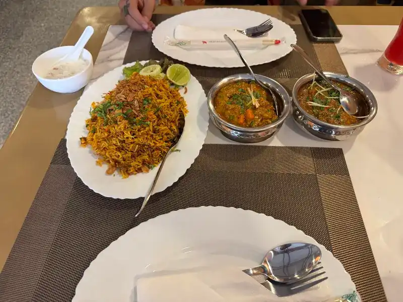 A plate of spiced rice beside two curries in steel bowls